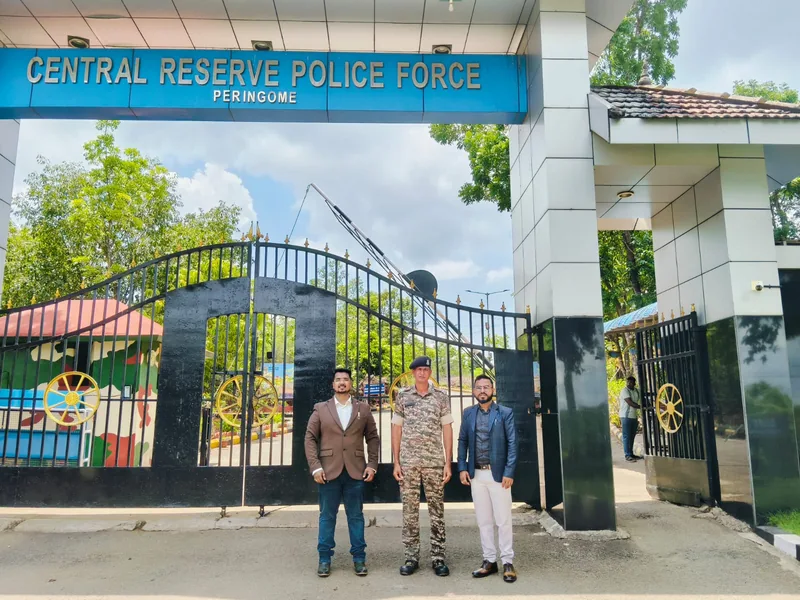Three people at the entrance gate of the Central Reserve Police Force campus at Peringome